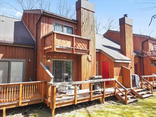 back of property with a deck, roof with shingles, and a chimney