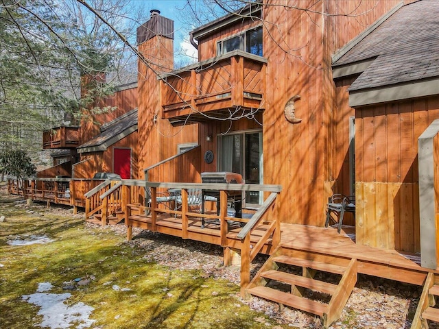 back of house with a wooden deck, a chimney, and a shingled roof