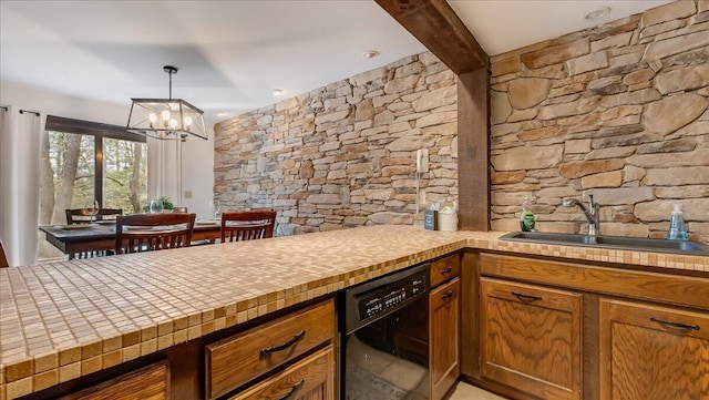 kitchen with brown cabinetry, a peninsula, a sink, light countertops, and black dishwasher