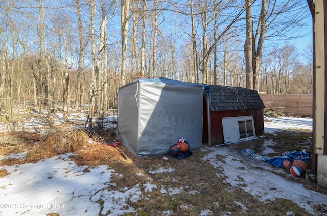 snow covered structure with an outdoor structure, fence, and a storage unit