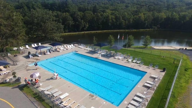 pool featuring a patio area, fence, a water view, and a wooded view