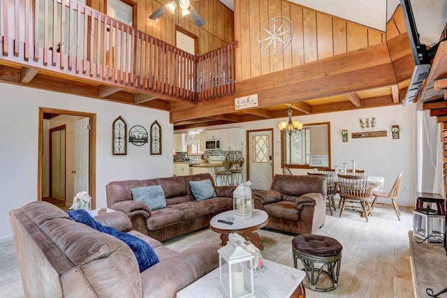 living room featuring beam ceiling, a high ceiling, ceiling fan with notable chandelier, and light wood-type flooring