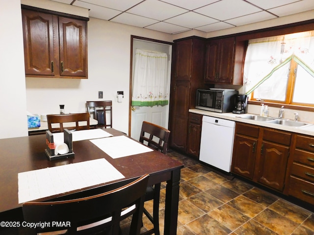 kitchen featuring black microwave, a drop ceiling, white dishwasher, and a sink