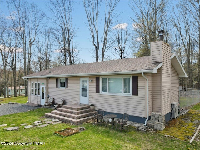 view of front of home with a front lawn, fence, a shingled roof, central AC unit, and a chimney