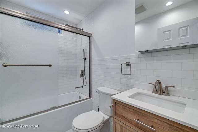 bathroom featuring tile walls, visible vents, toilet, combined bath / shower with glass door, and vanity