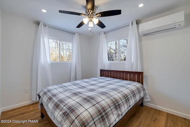 bedroom with an AC wall unit, multiple windows, baseboards, and wood finished floors