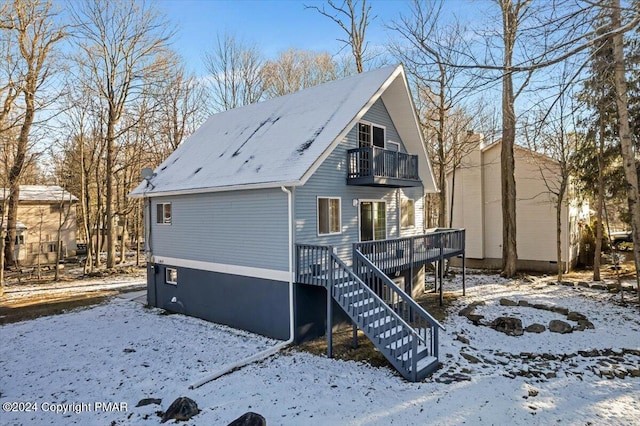 snow covered back of property featuring a balcony and stairway