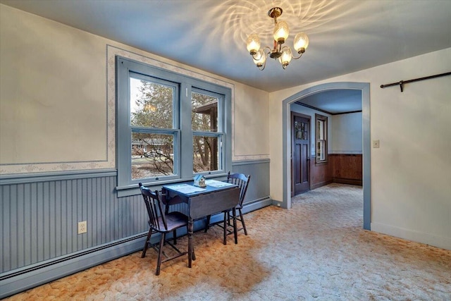 dining room with a baseboard heating unit, carpet, wainscoting, arched walkways, and a notable chandelier