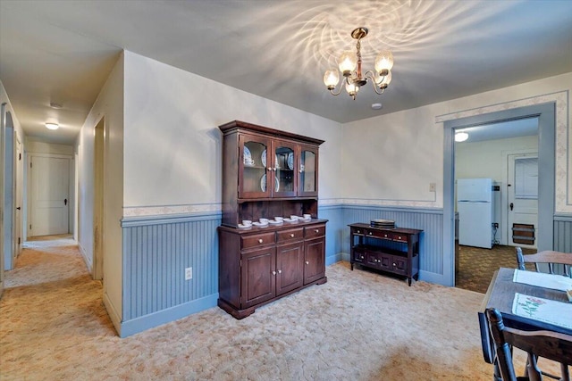 dining room with light carpet, wainscoting, and an inviting chandelier