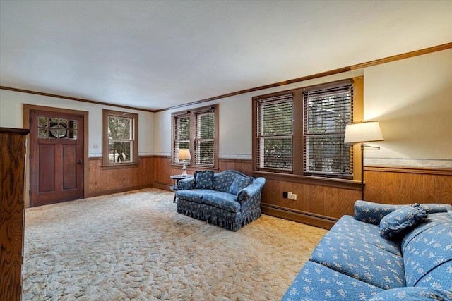 carpeted living room featuring baseboard heating, wainscoting, wooden walls, and ornamental molding