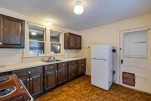 kitchen with dark brown cabinetry, freestanding refrigerator, electric range oven, and a sink