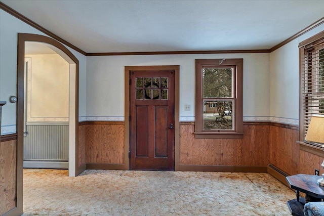 carpeted foyer featuring baseboard heating, wainscoting, and ornamental molding