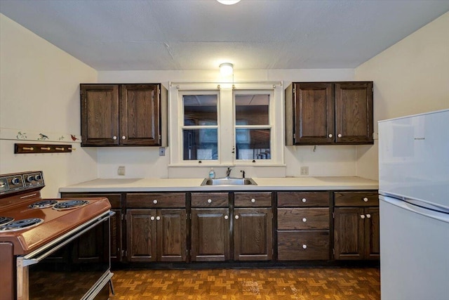 kitchen featuring dark brown cabinets, electric stove, freestanding refrigerator, and a sink