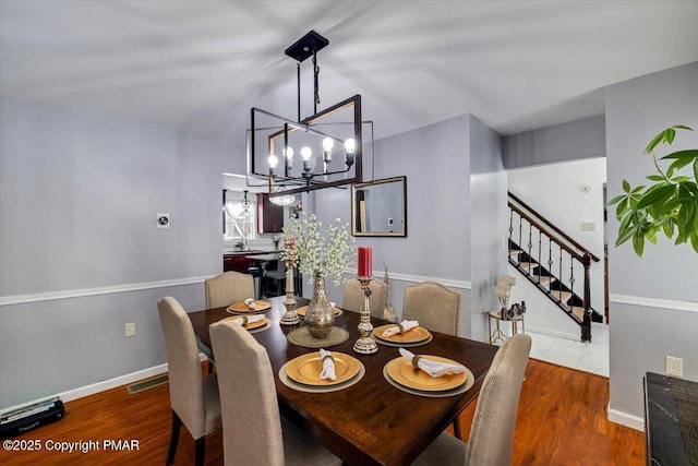 dining area with visible vents, baseboards, wood finished floors, an inviting chandelier, and stairs