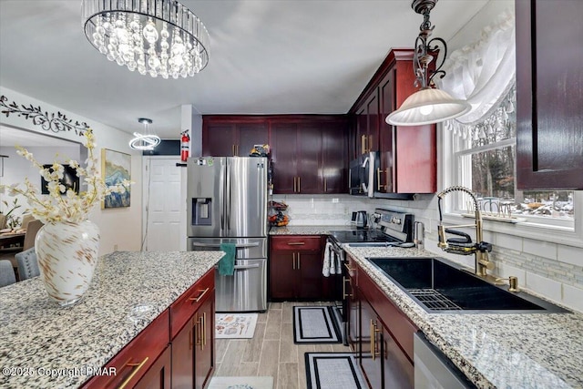 kitchen with appliances with stainless steel finishes, sink, pendant lighting, and light stone counters