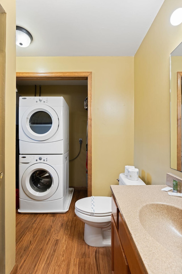 bathroom with toilet, vanity, stacked washer / dryer, and wood finished floors