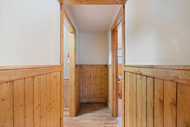 hallway with light wood finished floors, wood walls, and wainscoting