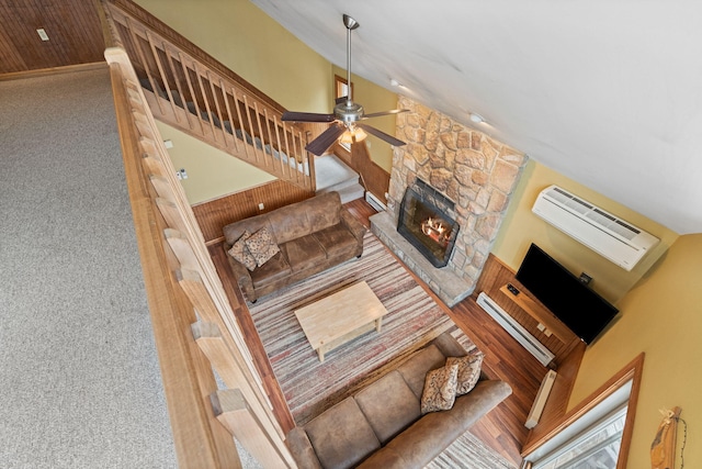 living area with a ceiling fan, a wall unit AC, stairway, vaulted ceiling, and a stone fireplace