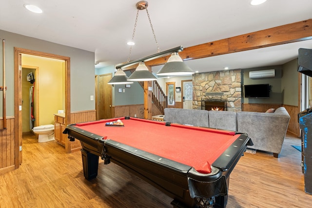 game room featuring a wainscoted wall, a stone fireplace, a wall mounted AC, and light wood-style flooring