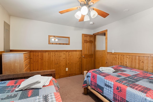 carpeted bedroom with wainscoting, a ceiling fan, and wooden walls