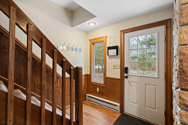 entryway with a baseboard heating unit, a wainscoted wall, wooden walls, and wood finished floors