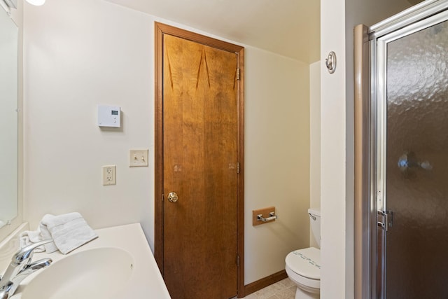 bathroom featuring a stall shower, a sink, toilet, and baseboards