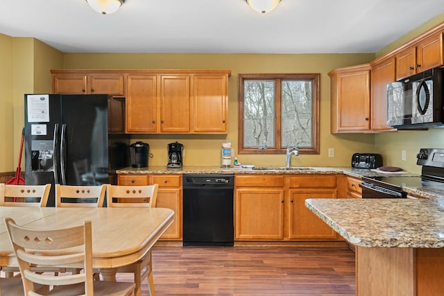 kitchen featuring light stone counters, a sink, light wood-style flooring, and black appliances