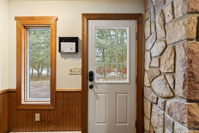 doorway to outside with a wainscoted wall, wood walls, and plenty of natural light