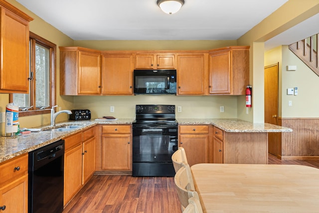 kitchen featuring dark wood-style flooring, a wainscoted wall, a sink, light stone countertops, and black appliances