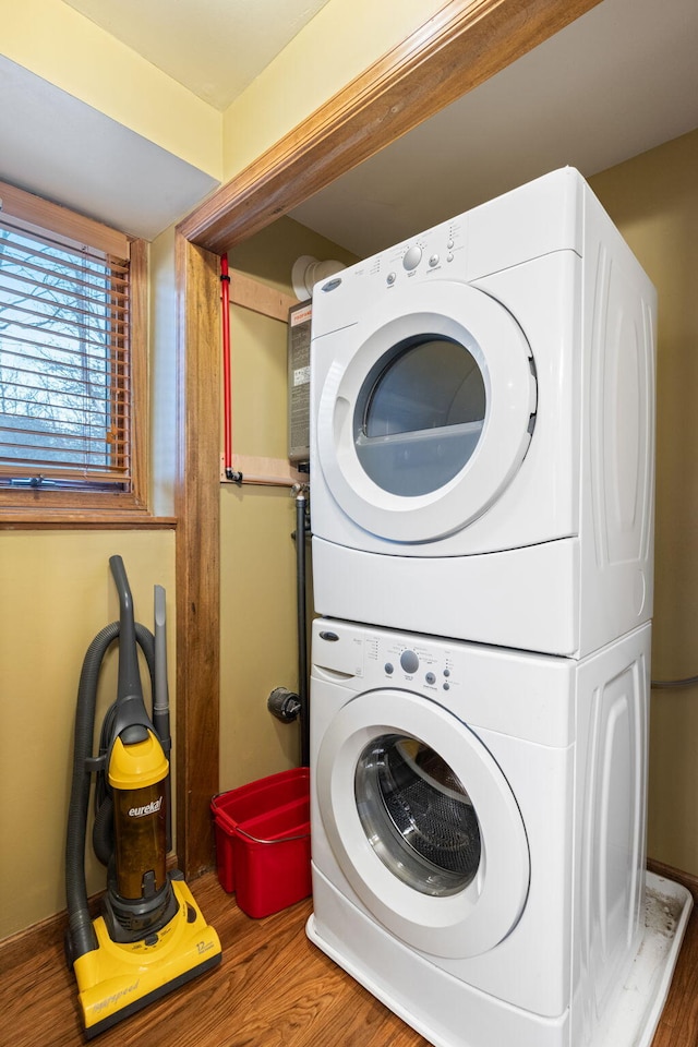 clothes washing area featuring stacked washing maching and dryer, laundry area, and wood finished floors