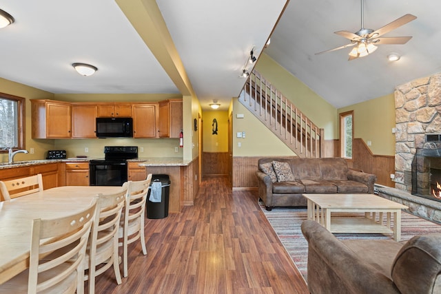 kitchen with a wainscoted wall, black appliances, a stone fireplace, and open floor plan