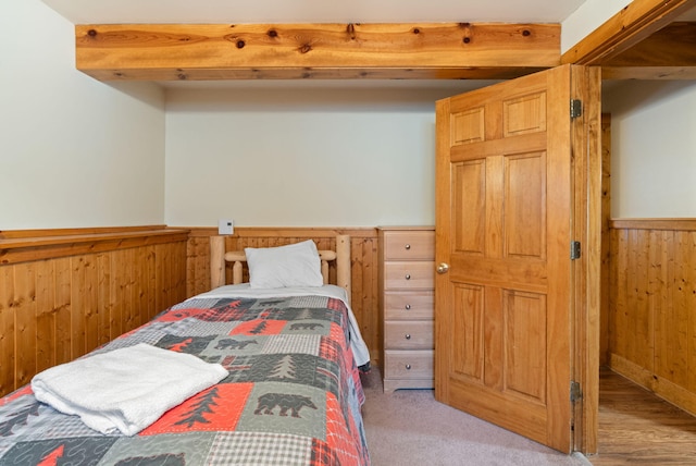 bedroom with wood walls, light colored carpet, and wainscoting