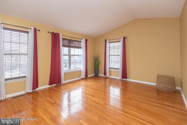 empty room with light wood-type flooring, baseboards, visible vents, and lofted ceiling