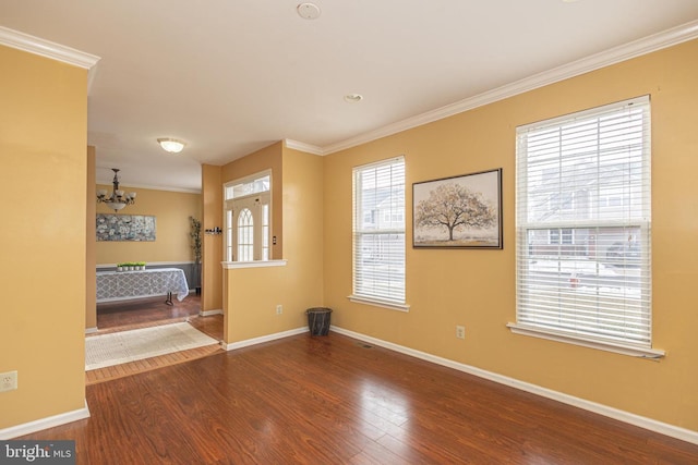 unfurnished room featuring an inviting chandelier, crown molding, baseboards, and wood finished floors