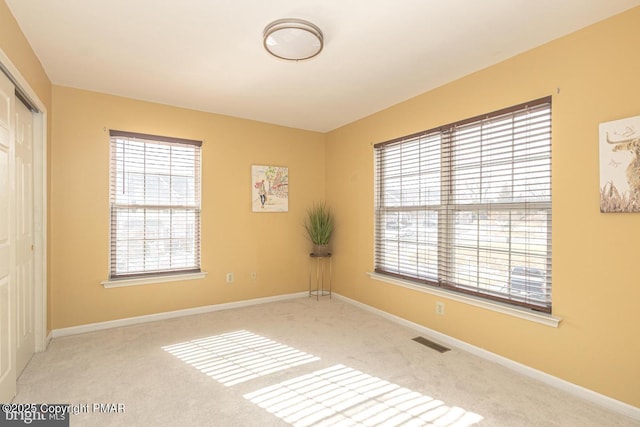 spare room featuring a wealth of natural light, carpet, visible vents, and baseboards