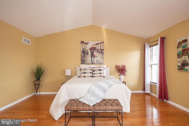 bedroom with vaulted ceiling, wood finished floors, visible vents, and baseboards