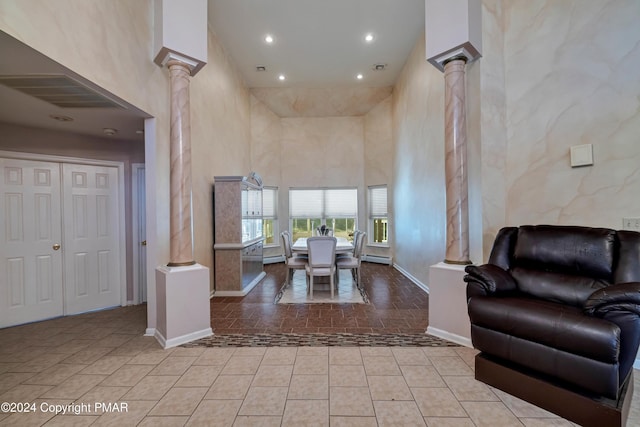 living area with baseboards, a high ceiling, tile patterned flooring, and ornate columns