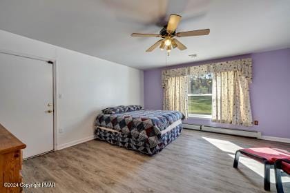 bedroom featuring a baseboard heating unit, ceiling fan, baseboards, and wood finished floors