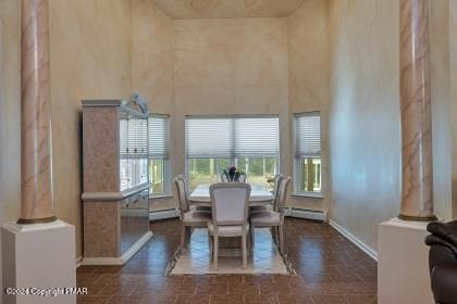 dining area with a baseboard heating unit, a baseboard radiator, a towering ceiling, and baseboards