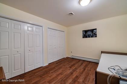 bedroom with dark wood-style flooring, baseboard heating, two closets, and visible vents