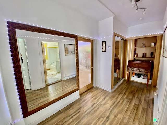 corridor featuring baseboard heating, light wood-style flooring, and rail lighting