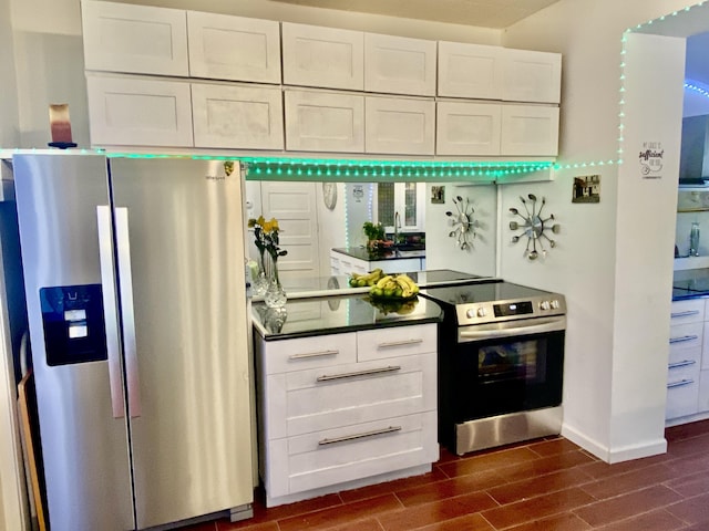 kitchen with dark countertops, baseboards, wood finish floors, appliances with stainless steel finishes, and white cabinets