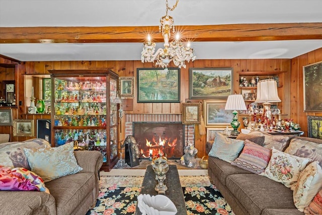 living room featuring wooden walls, beamed ceiling, a chandelier, and a brick fireplace