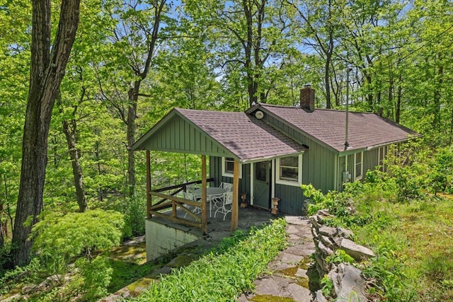 view of front facade featuring board and batten siding, a shingled roof, a hot tub, and a chimney