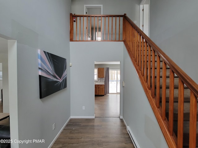 stairs with hardwood / wood-style flooring, baseboard heating, and a high ceiling