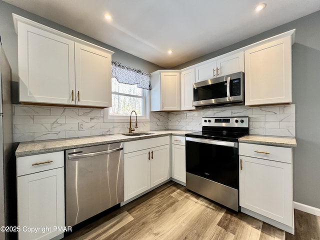 kitchen with stainless steel appliances, sink, white cabinets, and light wood-type flooring