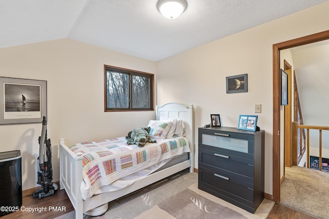 bedroom with vaulted ceiling, a textured ceiling, baseboards, and wood finished floors