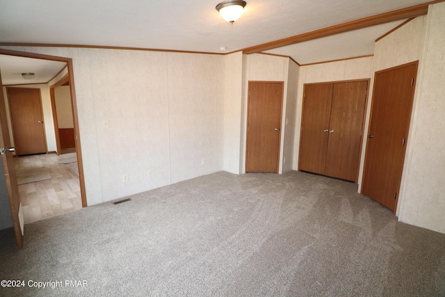 unfurnished bedroom featuring ornamental molding, carpet, visible vents, and multiple closets