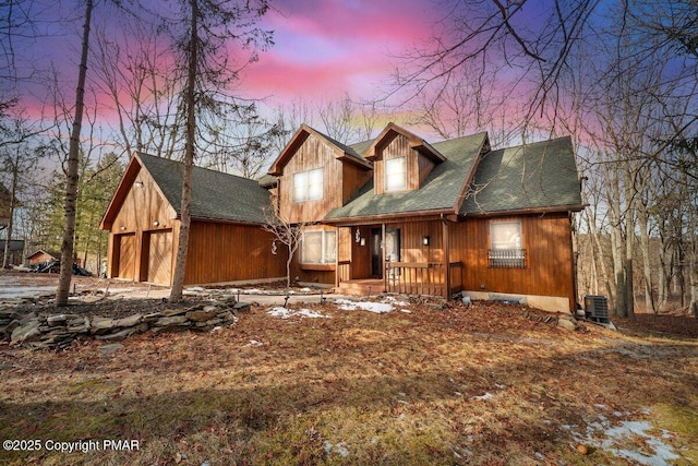 rustic home with cooling unit, covered porch, a garage, and roof with shingles