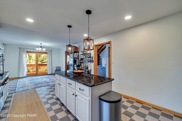 kitchen with an inviting chandelier, a center island, hanging light fixtures, dark stone counters, and white cabinets